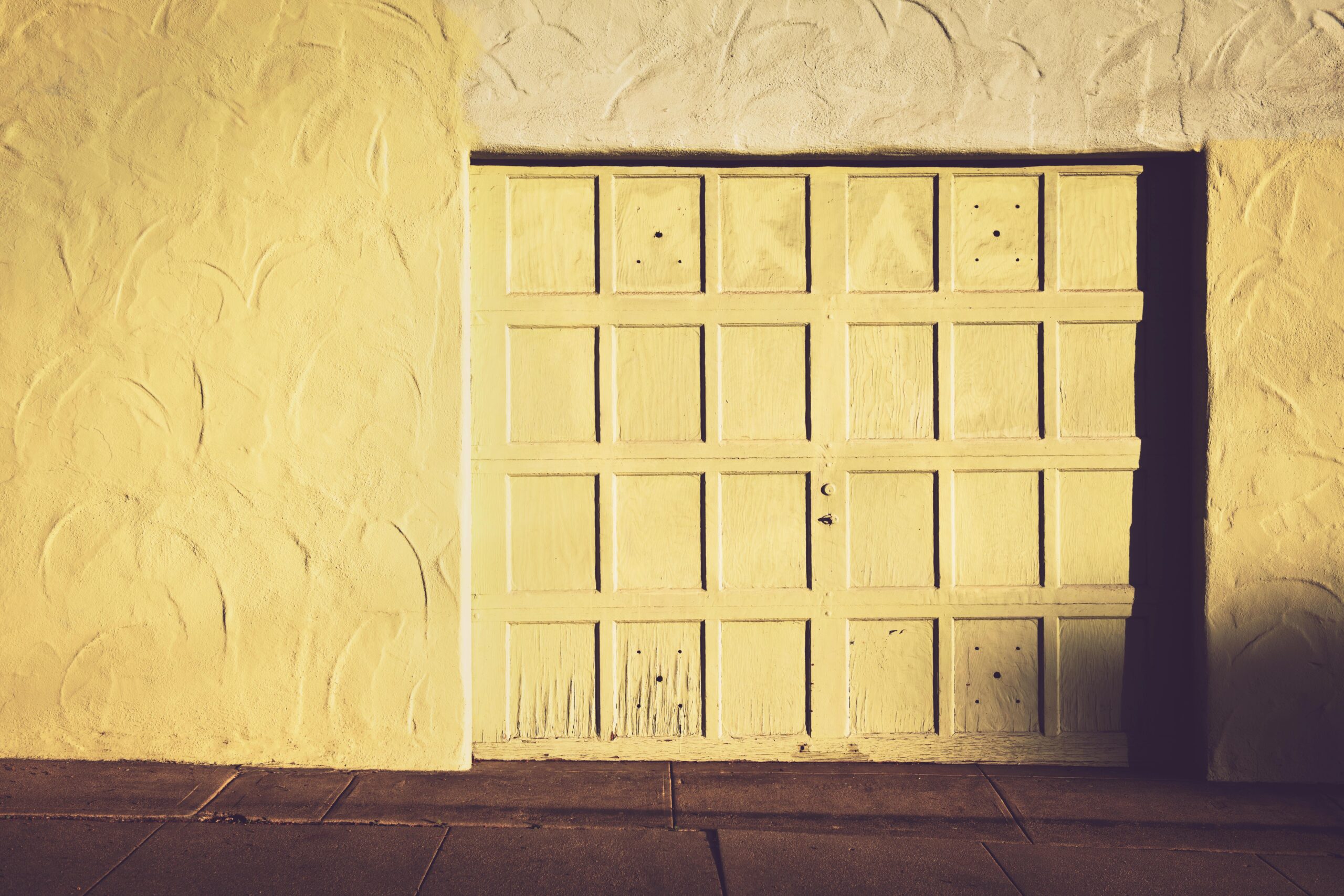A vintage wooden garage door set against a textured wall in warm, muted tones.